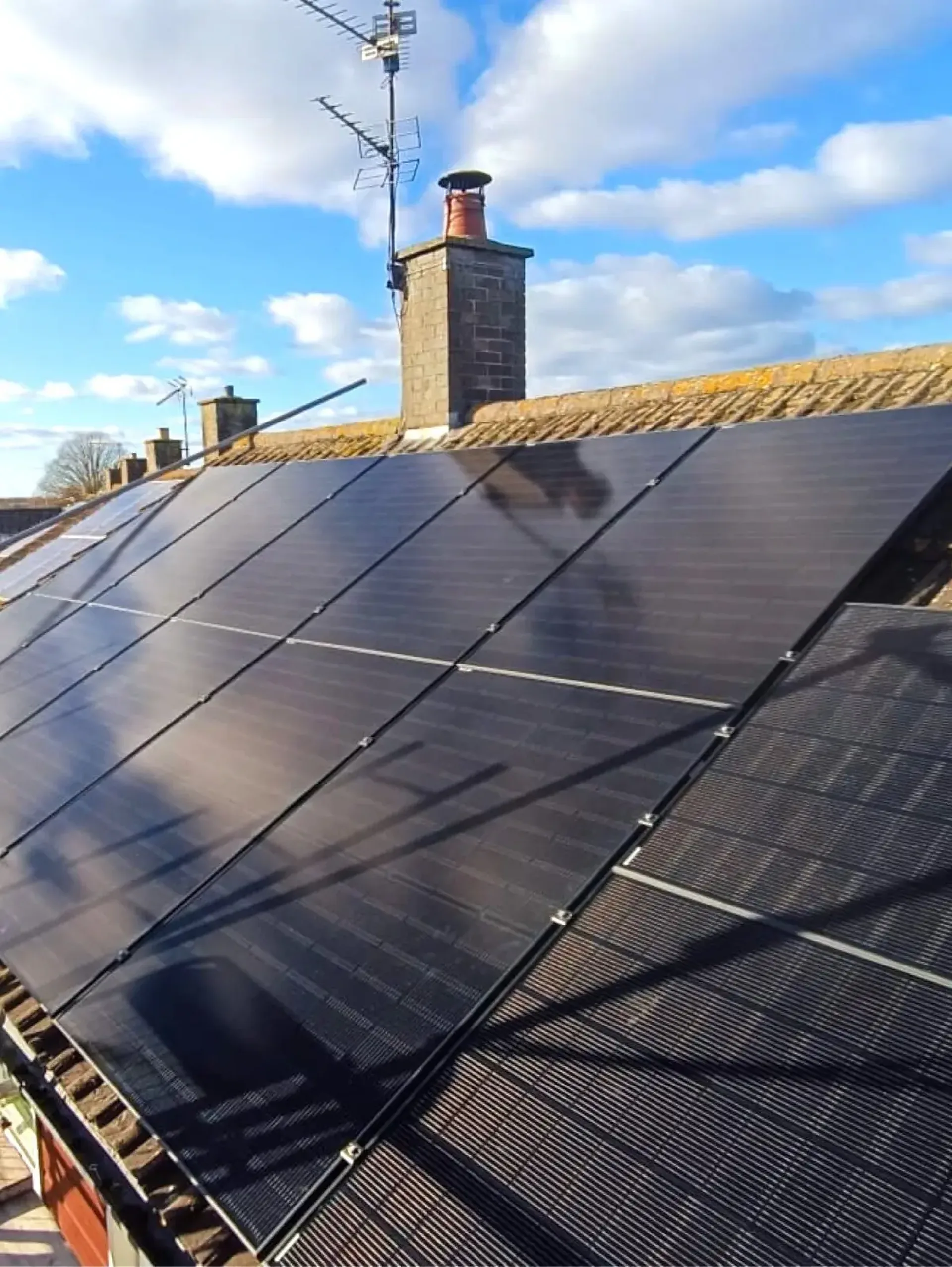 Rows of solar panels on a British terraced roof beside a brick chimney