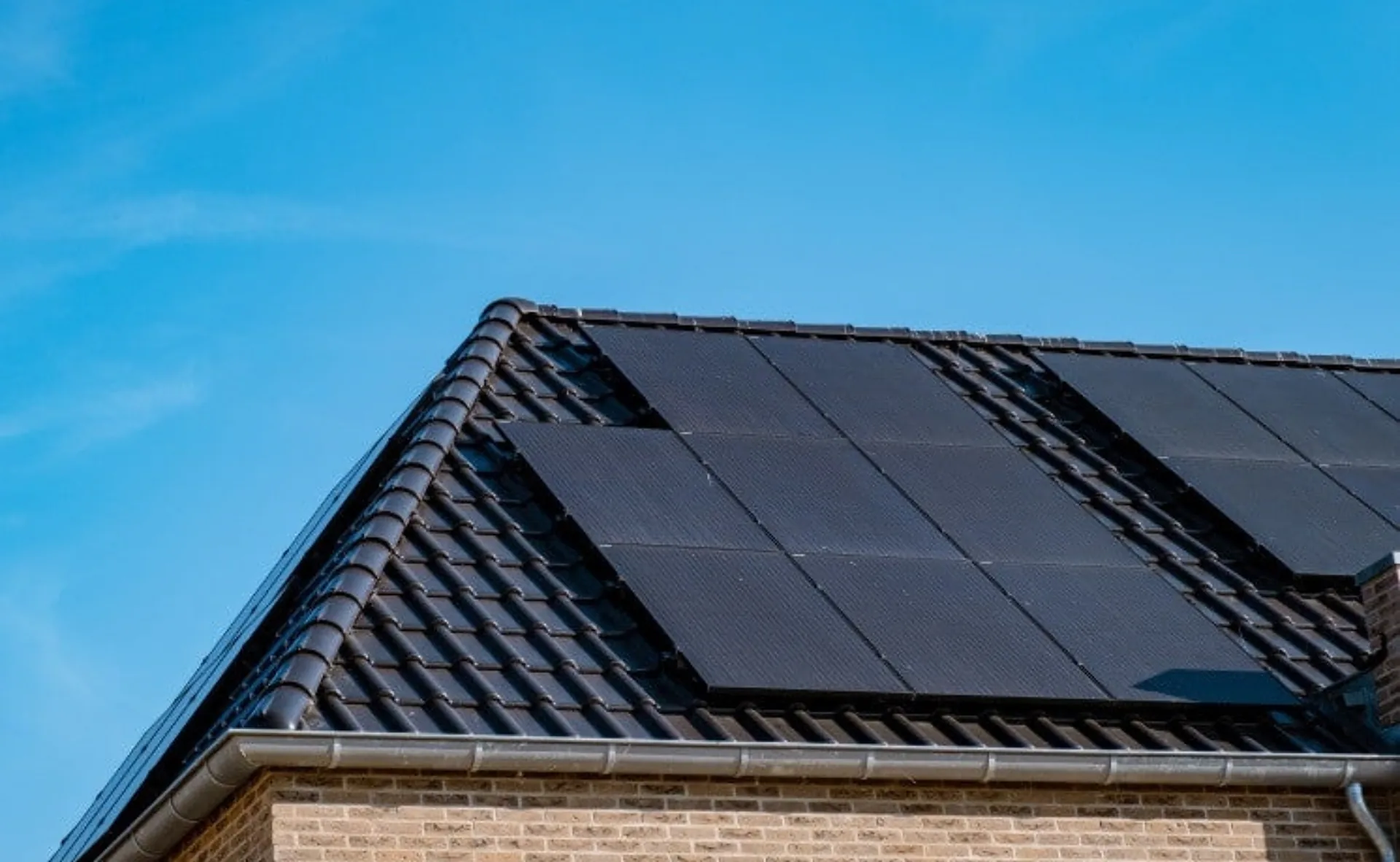 Solar panels on a dark tiled roof of a brick home against a clear blue sky